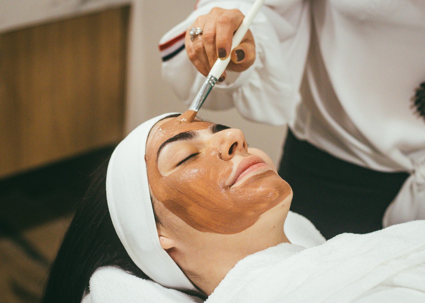 A beautician applying a facial mask to a relaxed customer at home